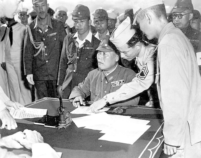 ABOARD USS DUNLAP (DD 384), off Chichi Jima, September 3, 1945: Lieutenant General Yoshio Tachibana, assisted by MIS Nisei Edwin Kawamoto, prepares to sign documents surrendering the Bonin Islands. (U.S. Navy photo)