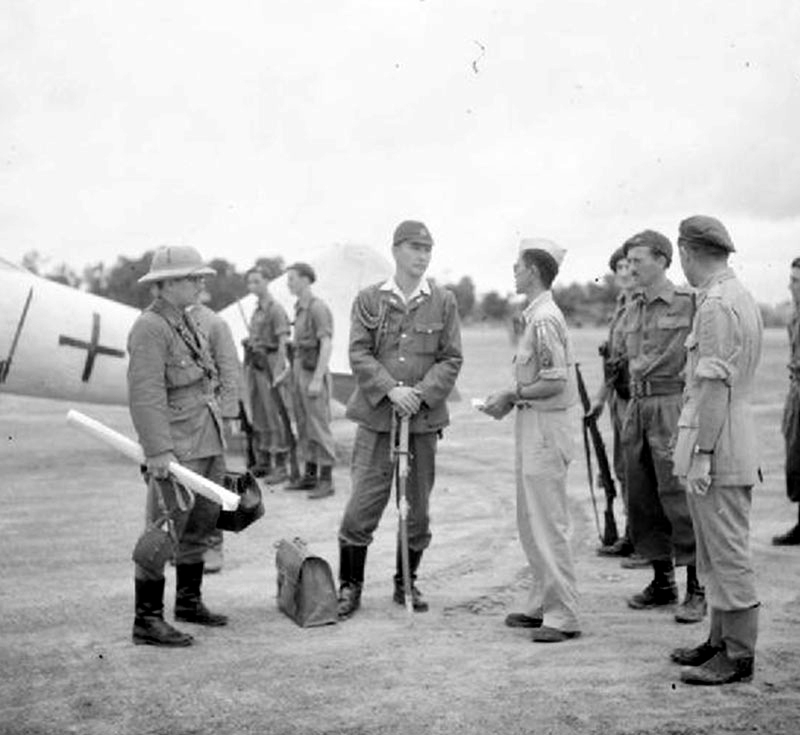 MINGALADON AIRFIELD, Burma, August 26, 1945: U.S. interpreter, right center, talks with Commander S. Kusumi of the Japanese delegation that arrived in specially marked aircraft to begin preliminary surrender negotiations for Japanese forces in South Burma.