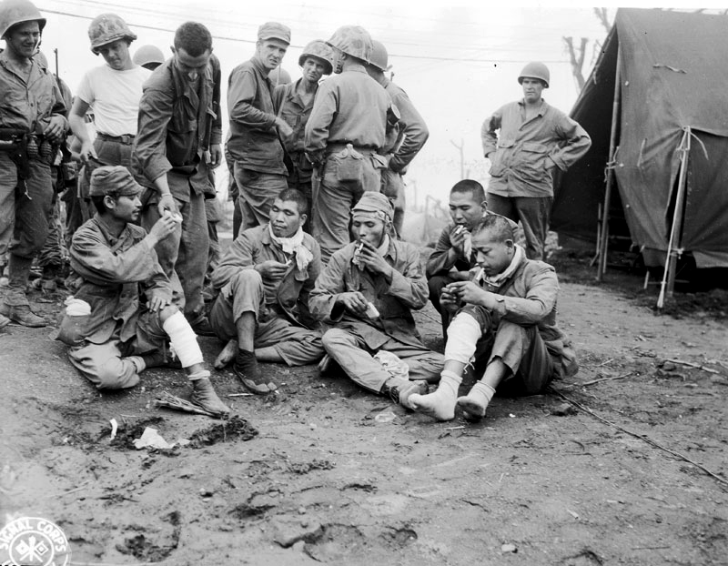 US soldiers offer cigarettes to captured Japanese soldiers.